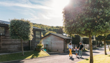 A family of three walking down a road on a lodge park surrounded by holiday lodges and woodland on a sunny, blue sky day