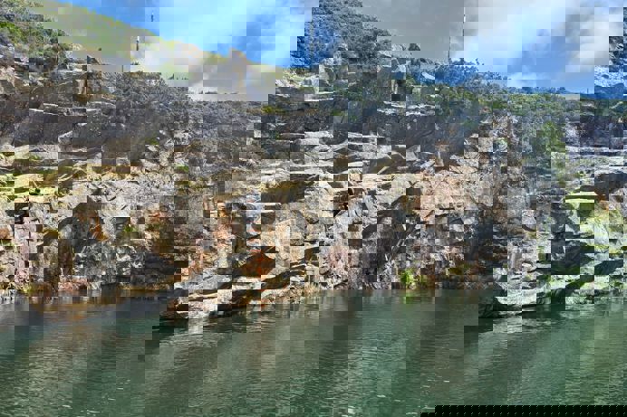 A quarry with a body of water in the centre and a person climbing a ladder up the rocks