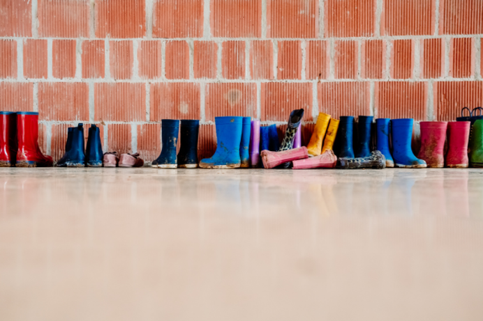 A bunch of wellington boots lined up against a wall in different colours and sizes