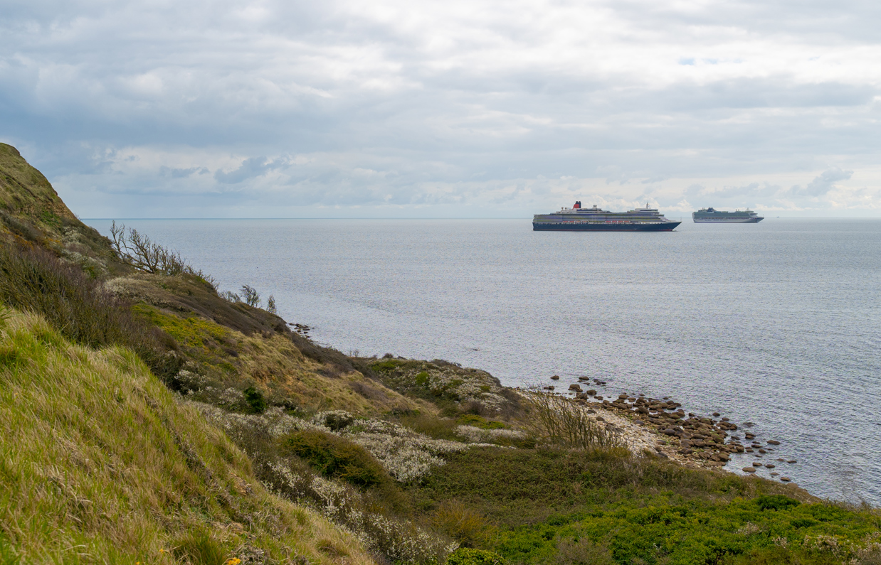 A seaview from a rocky cliff face with cruise ships in the distance on a cloudy day