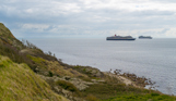 A seaview from a rocky cliff face with cruise ships in the distance on a cloudy day