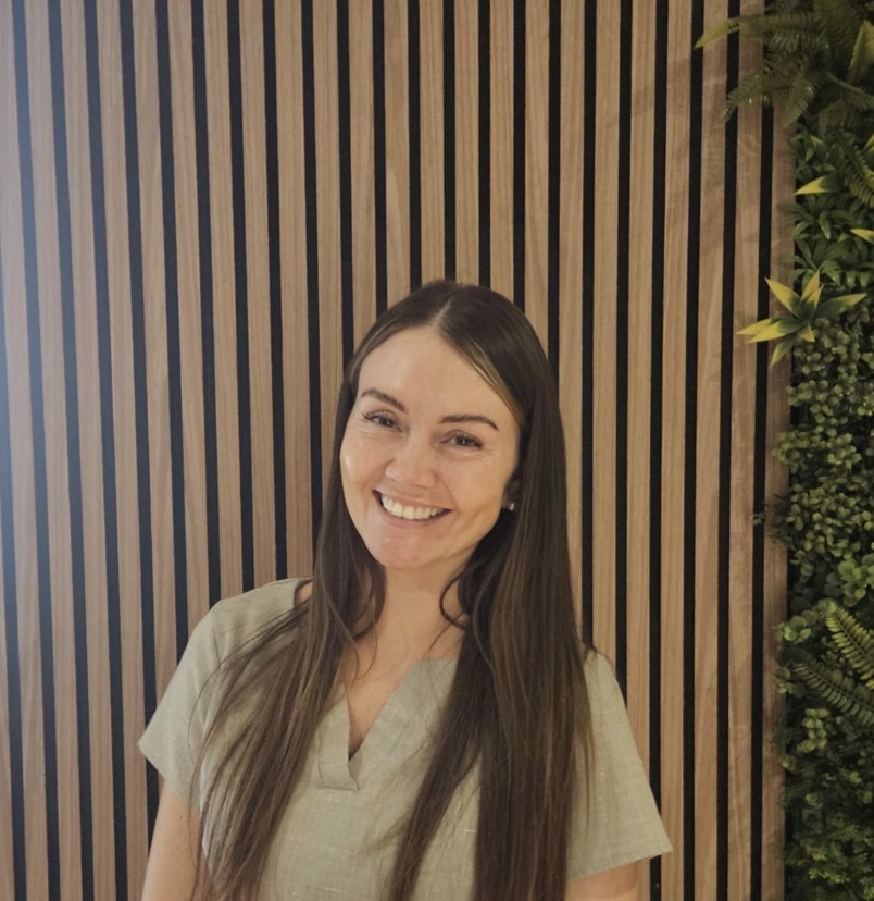 A lady smiling in spa uniform against a greenery / walnut decór background
