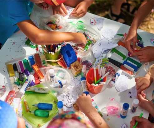A group of children gathered around a table doing arts and crafts taken from above