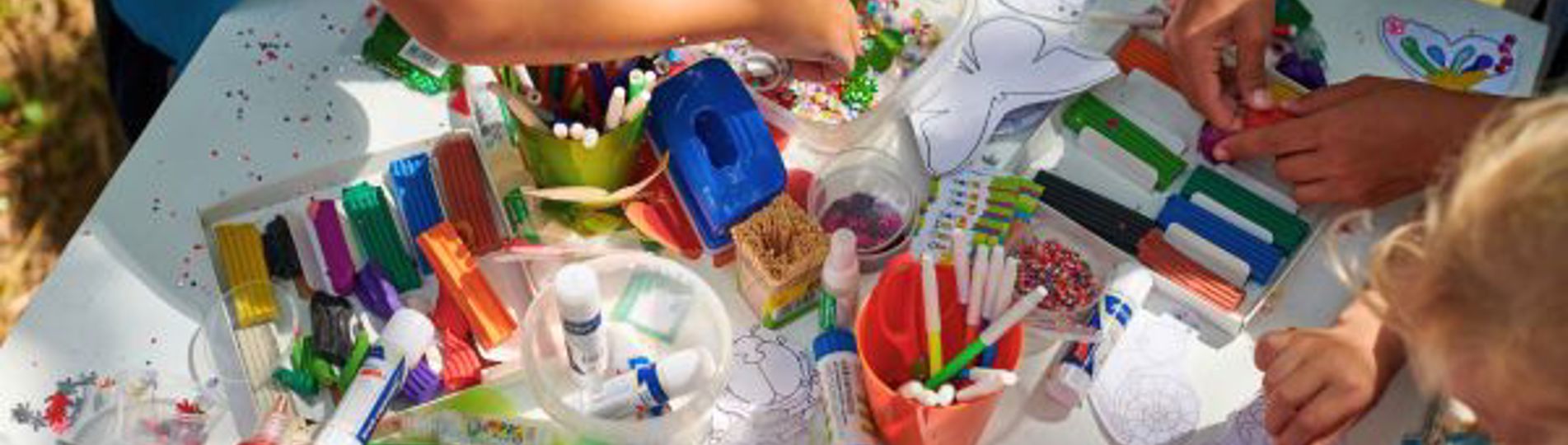A group of children gathered around a table doing arts and crafts taken from above
