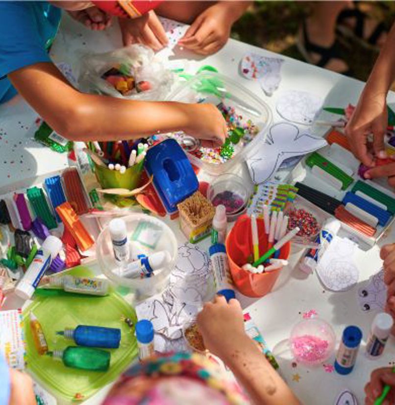 A group of children gathered around a table doing arts and crafts taken from above