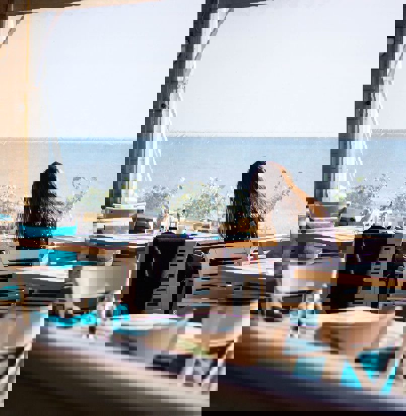 A woman sat at a table in a restaurant with sea views
