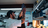 Two male chefs with tattoos in the kitchen of Drift Bar & Grill high fiving behind the serving counter after working together to plate up dishes