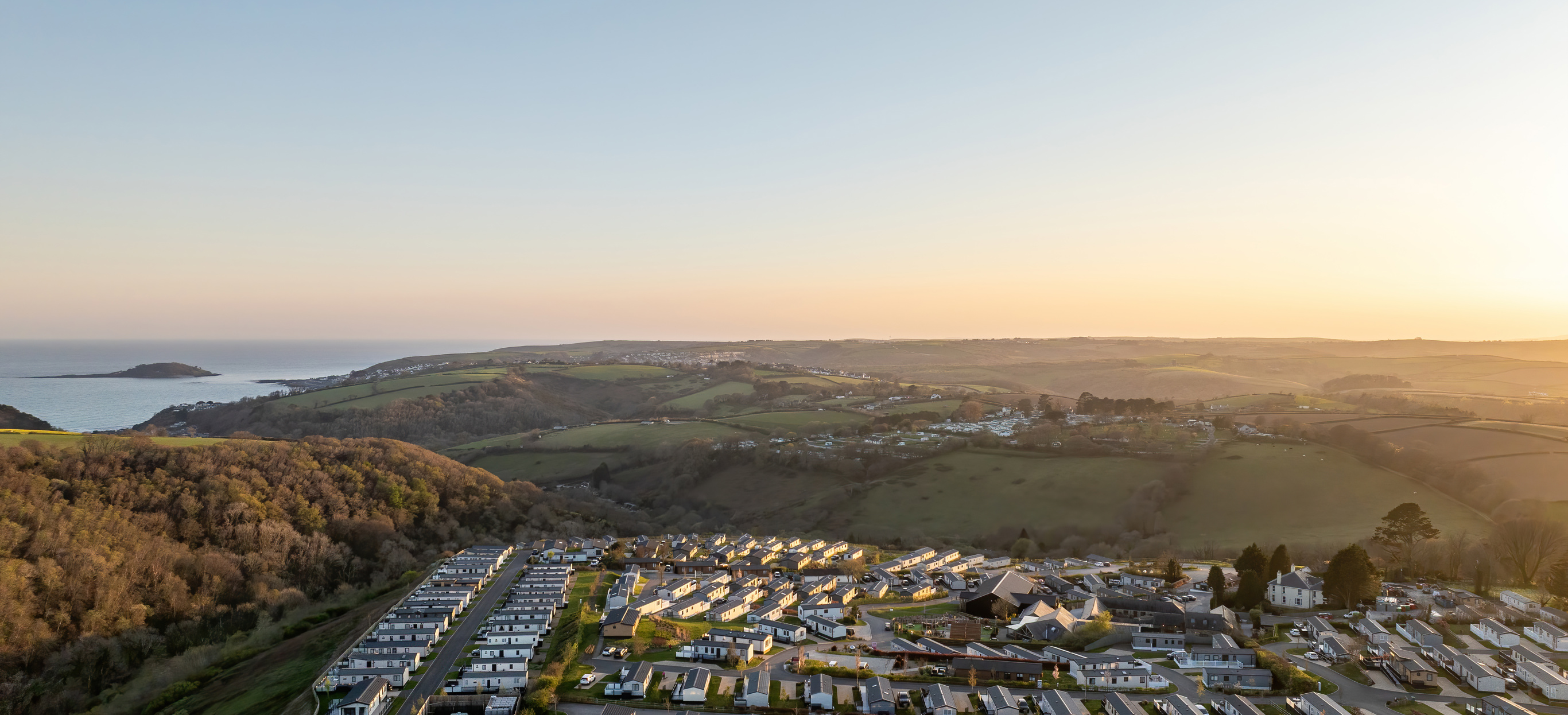 An aerial shot of Tregoad Holiday Park at sunset with views out to sea and Looe Island