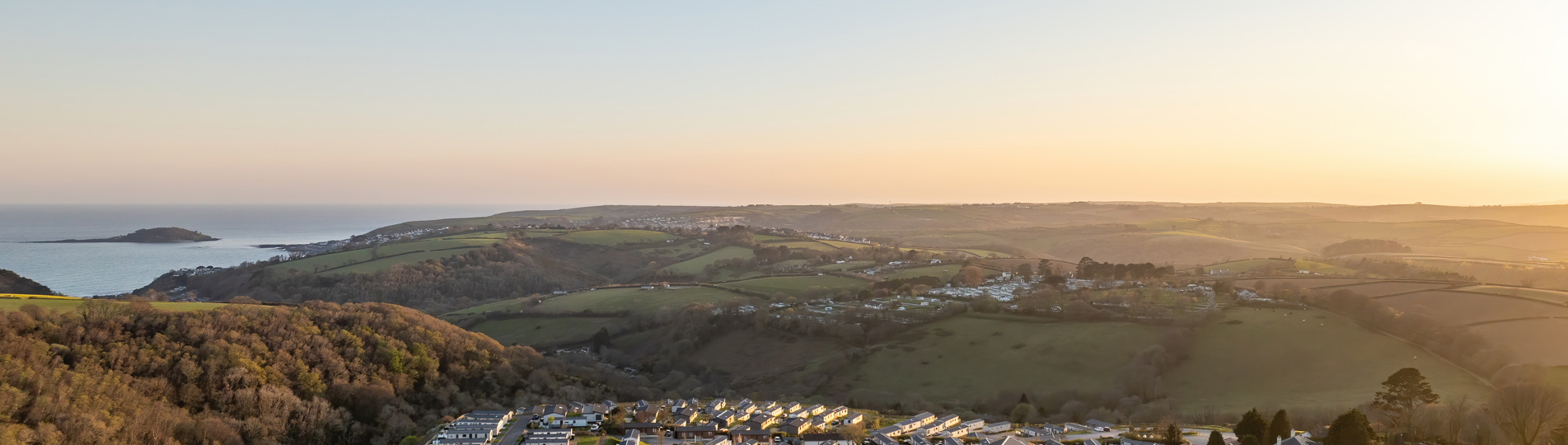 An aerial shot of Tregoad Holiday Park at sunset with views out to sea and Looe Island