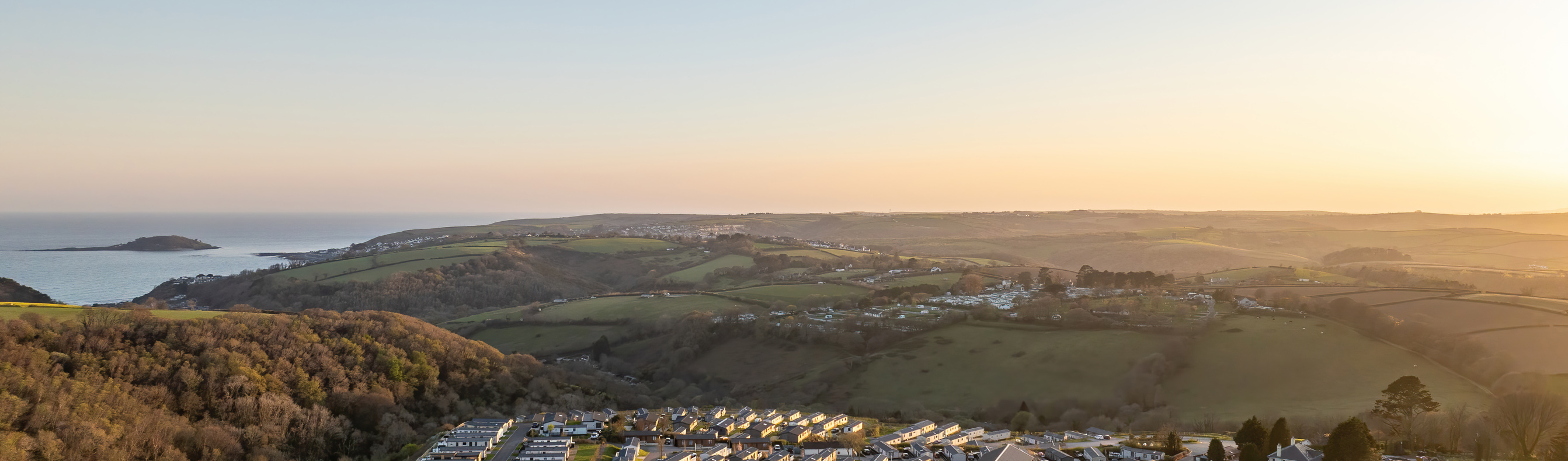 An aerial shot of Tregoad Holiday Park at sunset with views out to sea and Looe Island