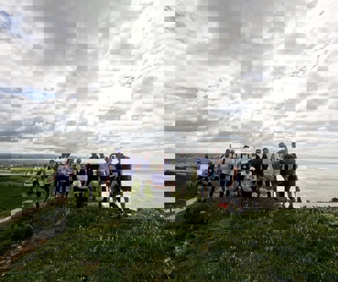 A group of people on the top of a cliffside on a walk looking out towards the sea