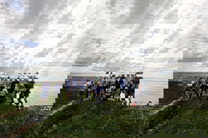 A group of people on the top of a cliffside on a walk looking out towards the sea
