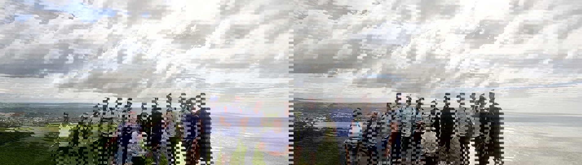 A group of people on the top of a cliffside on a walk looking out towards the sea