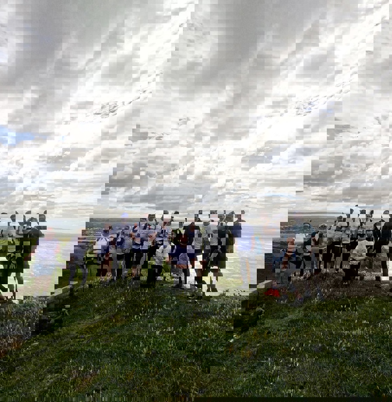 A group of people on the top of a cliffside on a walk looking out towards the sea
