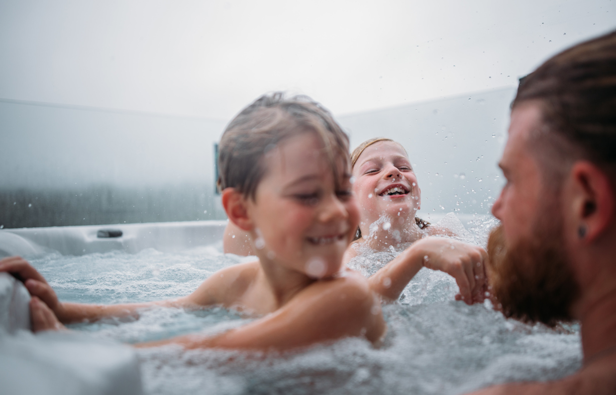 Two young boys and a man playing in a hot tub at Tregoad Holiday Park on a cloudy day