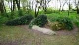 A bigger than life size stone sculpture of a human laying down with greenery growing over it to mimic clothing and hair