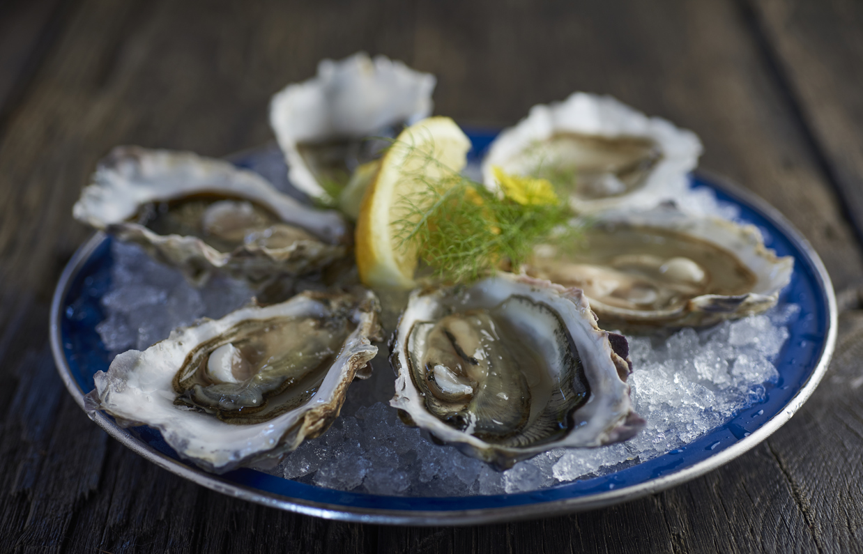 A plate of oysters on a bed of crushed ice with lemon and garnish