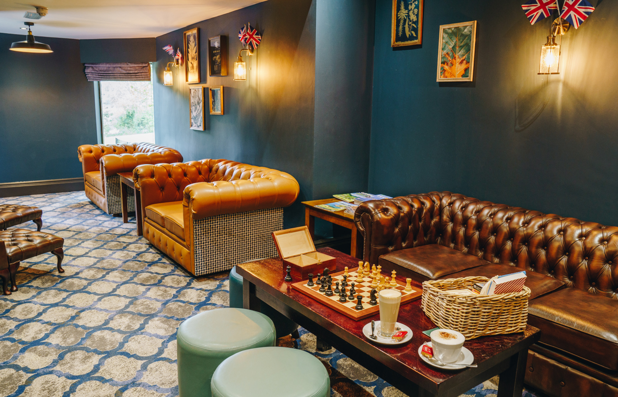 A snug style, moody decor games room with sofas, tables, chess, other games and books as well as coffees
