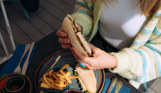 A filled baguette being held by a lady above a plate of chips 