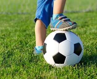 A young child's feet one of which is upon a football on grass