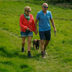 A couple holding hands walking through a field with their dog