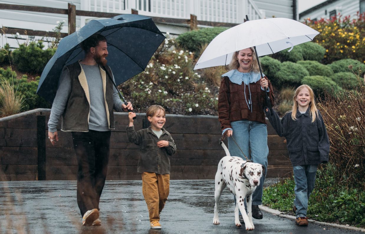 A family of four walking in the rain with umbrellas and a dalmatian