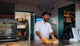 A male server at a street food shack smiling serving some food across the counter