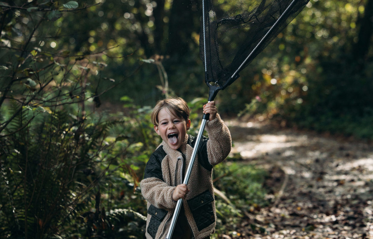 A young boy holding a fishing net up vertically with his tongue out