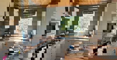 Open plan kitchen with island in sage colour theme and natural wood worktops