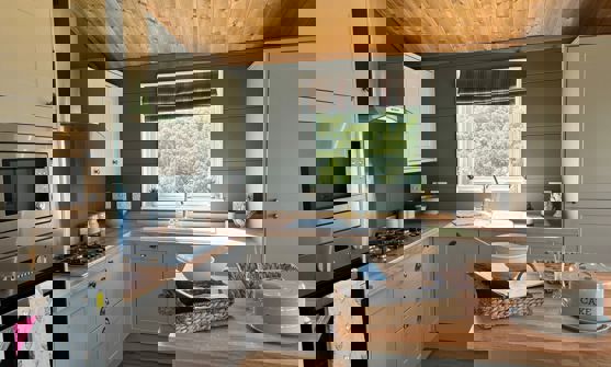 Open plan kitchen with island in sage colour theme and natural wood worktops