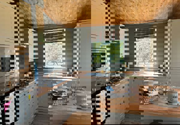 Open plan kitchen with island in sage colour theme and natural wood worktops