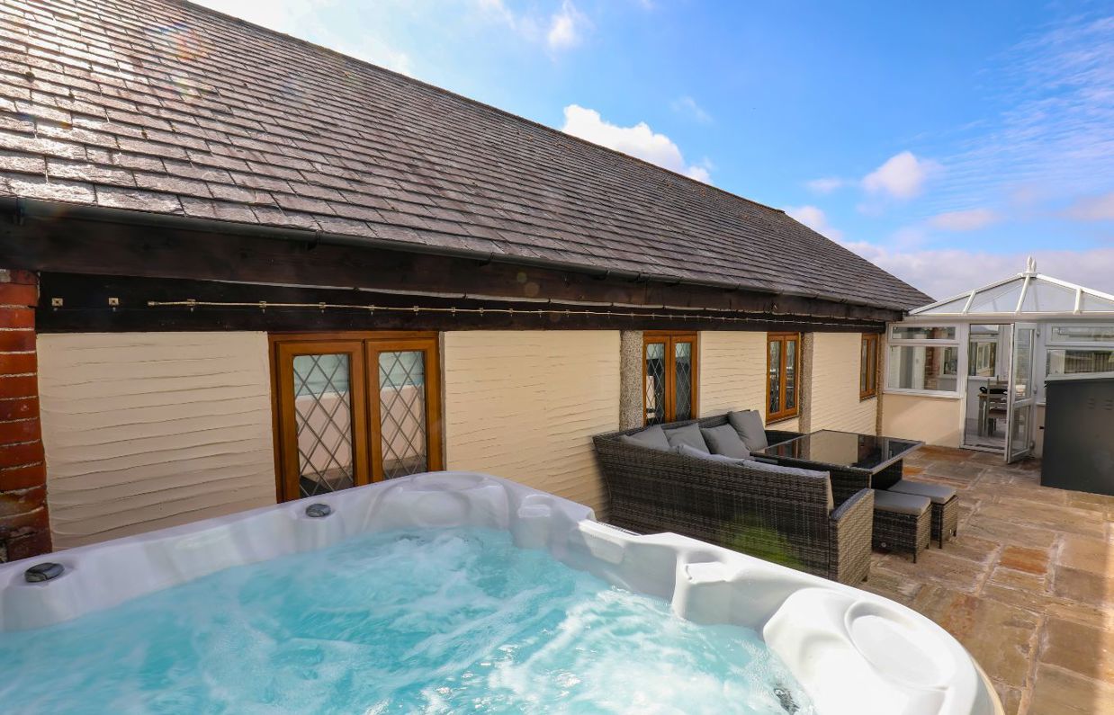 External of a cottage outside area with hot tub, conservatory and outdoor furniture