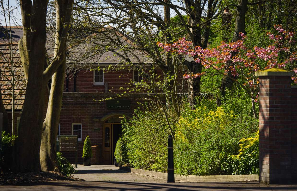 The entrance to The Country Club among countryside, trees and flowers