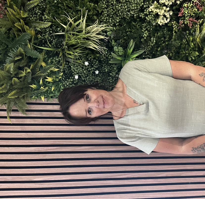 A lady smiling in spa uniform against a greenery / walnut decór background