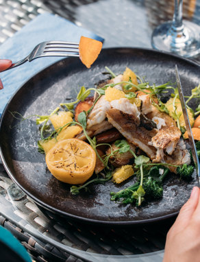 A fish dish on a black plate being eaten outside at a table