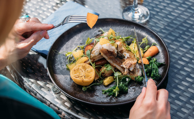 A fish dish on a black plate being eaten outside at a table
