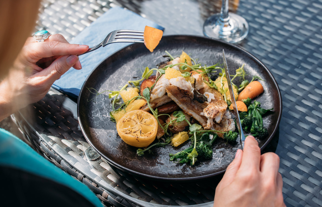 A fish dish on a black plate being eaten outside at a table