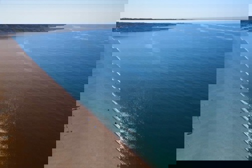 Aerial view of a stretch of Chesil Beach looking out towards the blue sea and Portland