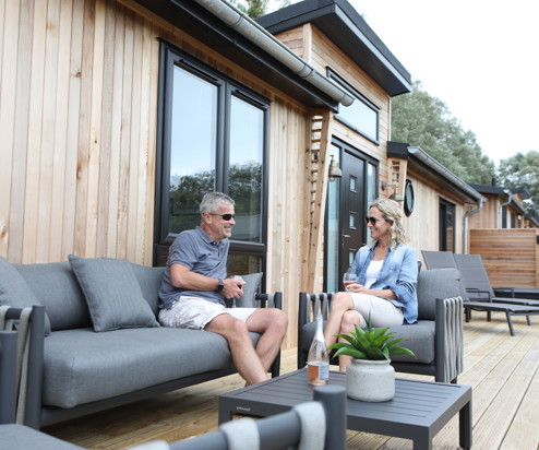 A couple sat on outdoor furniture on the decking of a lodge