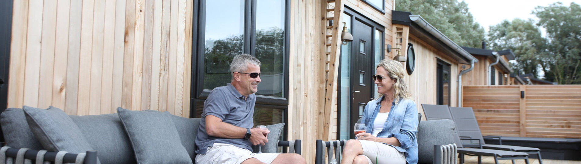 A couple sat on outdoor furniture on the decking of a lodge