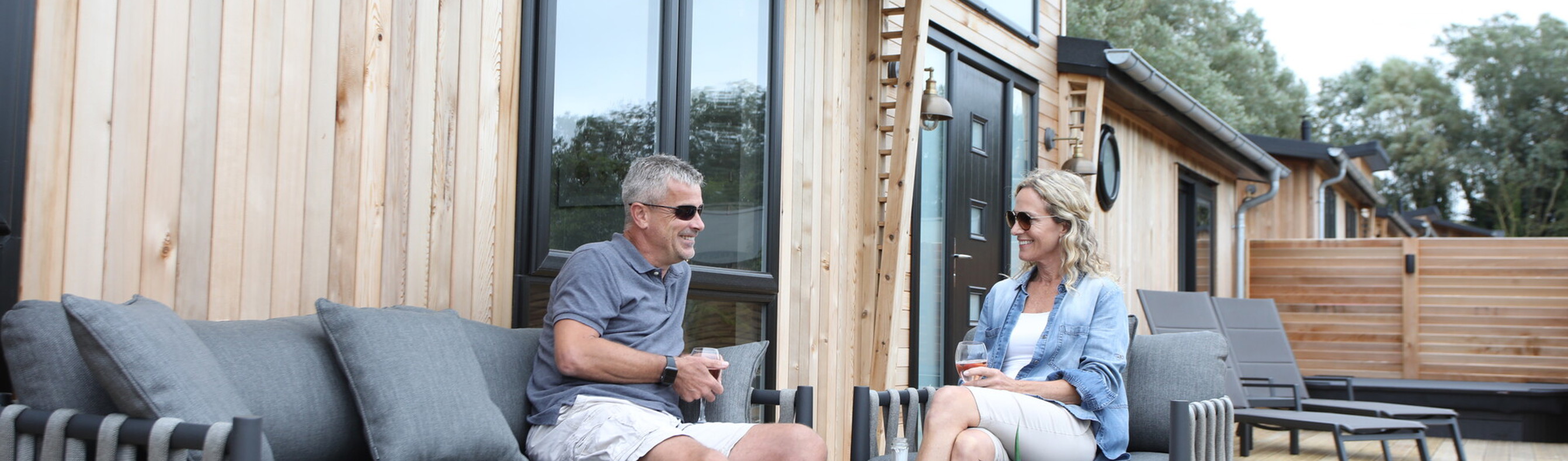 A couple sat on outdoor furniture on the decking of a lodge