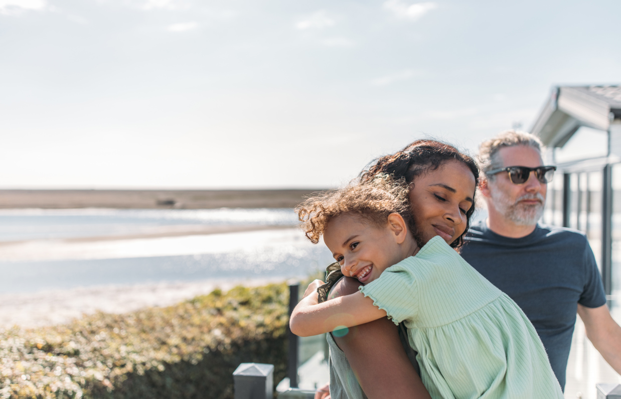 Mother and daughter cuddle while family enjoy view from deck at Chesil Beach