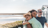 Mother and daughter cuddle while family enjoy view from deck at Chesil Beach
