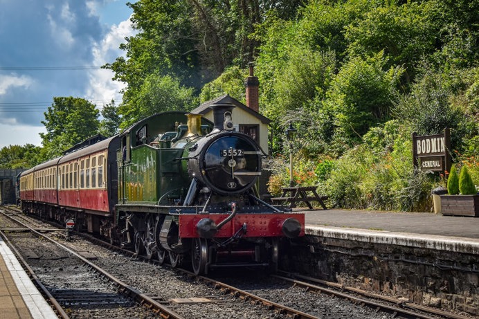 An old fashioned steam train at Bodmin station among trees and greenery