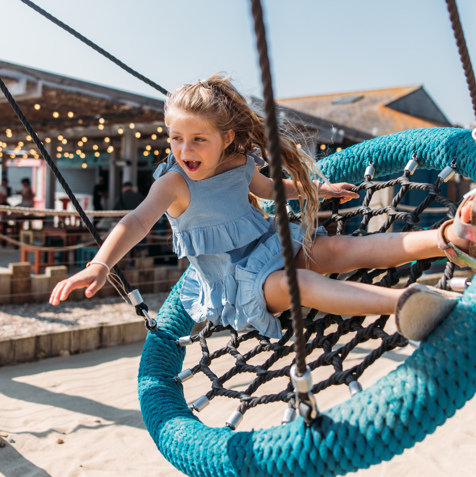 A young girl playing on a swing at an outdoor play park
