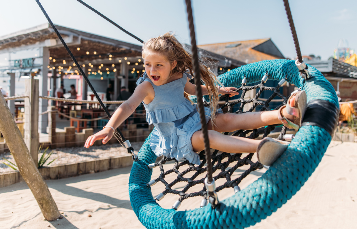 A young girl playing on a swing at an outdoor play park