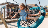 A young girl playing on a swing at an outdoor play park