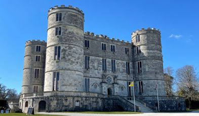 A stunning large castle on a blue sky day with multiple floors and turrets
