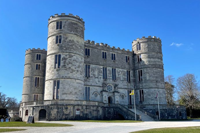 A stunning large castle on a blue sky day with multiple floors and turrets