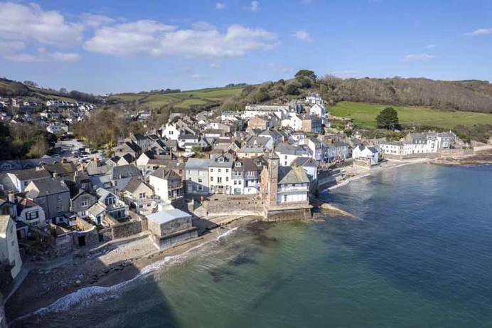 A small coastal town by the sea with blue waters and rolling hills in the background on a sunny, blue sky day
